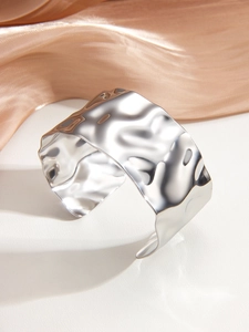 Detail of wide open cuff bracelet with irregular silver wave texture and high-gloss metallic finish