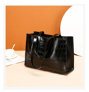 Detail view of black crocodile pattern tote bag with long straps on minimalist decor