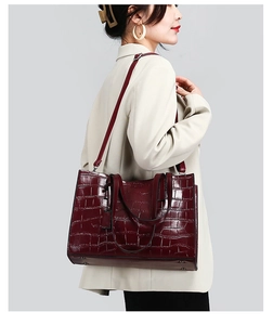 Detail view of burgundy crocodile pattern handbag showing high-gloss texture and metal studs