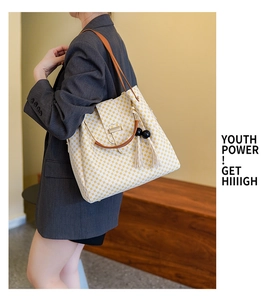 Detail of beige checkered tote bag featuring brown leather straps and pompom keychain