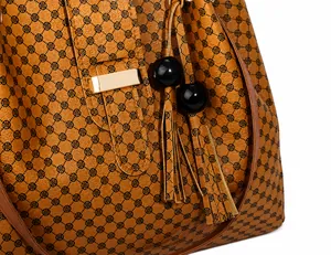 Detail of tan tote bag with vintage circular pattern, gold buckle and tassel charm