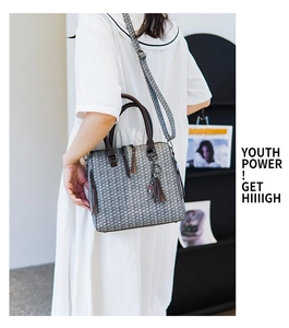 Detail of grey woven tote bag with dark brown leather straps and decorative tassel