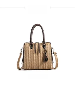 Front view of khaki woven handbag with dark brown handles and cat tassel charm detail