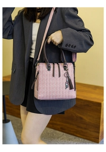 Close-up of a pink woven texture handbag with brown leather straps and a cat charm detail