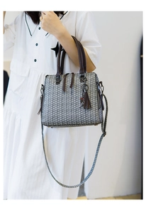 Detail of woven texture handbag with dark brown leather handles and decorative tassel pendant