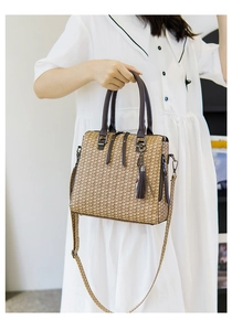 Detail of straw handbag featuring dark brown leather handles and a decorative tassel charm