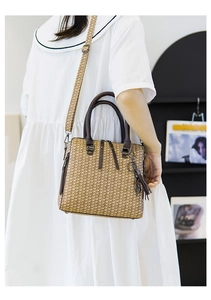 Detailed view of woven straw tote bag featuring brown leather straps and tassel charm