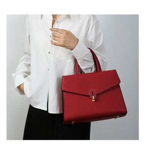 Detail of red lychee grain leather handbag featuring elegant gold oval buckle and flap closure