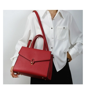 Detail of red textured leather handbag featuring a gold hardware lock and top handles