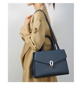 Navy blue top handle bag with pebble texture and metallic buckle shown on a trench coat