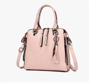 Vista laterale di borsa intrecciata rosa con nappa decorativa e ciondolo a gatto