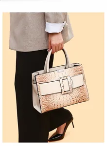 Beige crocodile pattern tote bag with large square buckle shown with a plaid suit