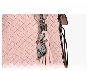 Dettaglio borsa intrecciata rosa con ciondolo a gatto in metallo e nappa decorativa