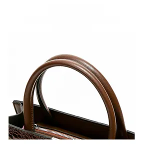 Detail of dark brown crocodile pattern handbag with sturdy round handle and silver zipper