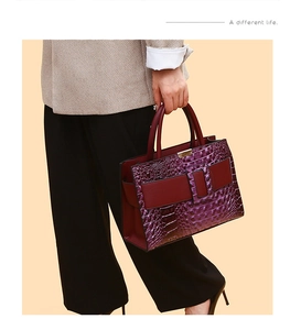 Detail of burgundy tote bag featuring embossed crocodile pattern and decorative buckle