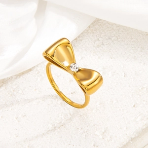 Eleganter goldener Schleifenring mit zentralem Zirkon auf weißem Steinuntergrund
