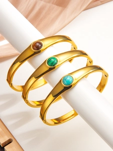 Détail de trois bracelets joncs vintage dorés ornés d'œil de tigre et de malachite