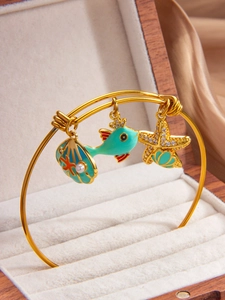 Detailed close-up of shell, starfish, and fish charms on a gold ocean-themed bracelet