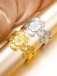 Detailed view of floral relief bangles in gold and silver on a luxury display stand
