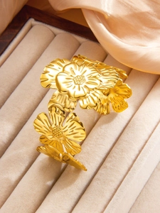 Detailed close-up of golden floral embossed bangle with textured petals on satin background