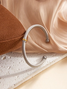 Detailed shot of silver cable wire bracelet with gold bead accent on marble background