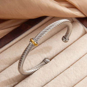 Minimalist cable twist bangle in silver and gold finish resting on a beige velvet gift box