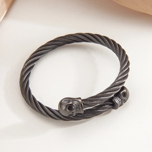 Punk style matte black cable wire bracelet with skull ends on white leather surface