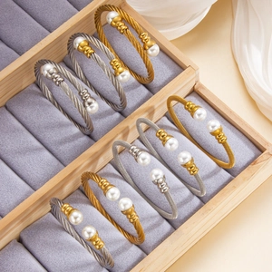 Vista dettagliata del set di bracciali a cavo con perle bianche e dettagli in oro 18k