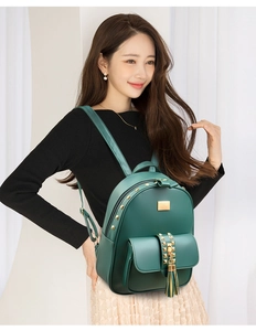 Detail view of dark green backpack with golden studs, fringe charm and metal plate