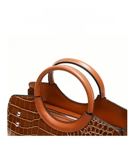 Close-up of brown crocodile pattern handbag showing reinforced stitching and metal rivets
