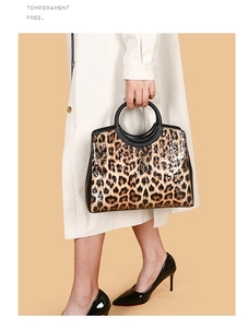 Detail of leopard print glossy handbag with large black circular handles worn with white coat