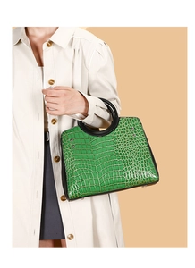 Detail of green crocodile embossed handbag with unique black circular resin handle