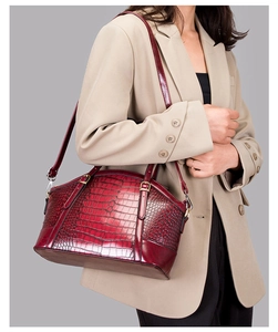 Detail of burgundy crocodile-embossed handbag with gold hardware on beige blazer