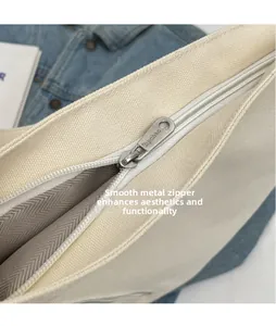 Detail of polished metal zipper pull with branding on a cream canvas shoulder bag