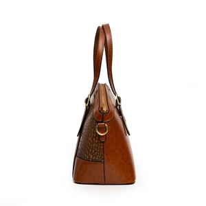 Brown leather handbag with crocodile pattern side panels and golden zipper in side view