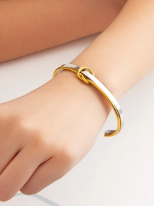Close-up of a two-tone knotted stainless steel bangle with polished gold and silver finish