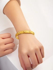 Detail of adjustable gold star bangle with brushed texture and zircon star charms