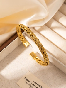 Macro detail of gold-plated braided steel bangle on silk fabric in jewelry box
