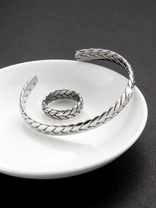 Vista detallada de la pulsera abierta con patrón de espiga y anillo de metal plateado