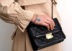 Detail of silver snake chain bracelet with sparkling blue evil eye charm on black leather bag