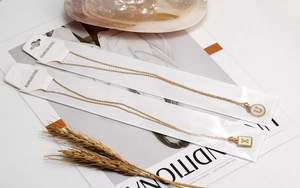 Detalle de colgantes de letras en acero inoxidable chapado en oro 18K con esmalte blanco