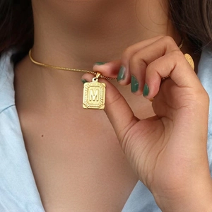 Close-up of a 18K gold plated stainless steel square pendant with letter M engraving