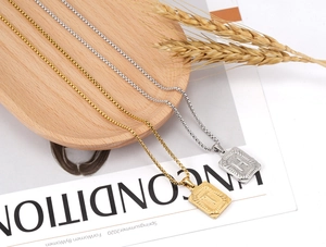 Close-up of gold and silver square letter pendants with sunburst texture on box chains