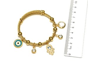Detail of gold-plated wire bracelet with Hamsa and Evil Eye charms next to a ruler