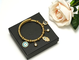 Macro detail of gold cable bangle with Hamsa Hand, Evil Eye, and crystal charms