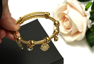 Detail of golden steel wire bracelet with Hamsa Hand and Evil Eye charms