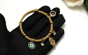 Detail of gold woven steel wire bracelet with evil eye and Hamsa hand charms
