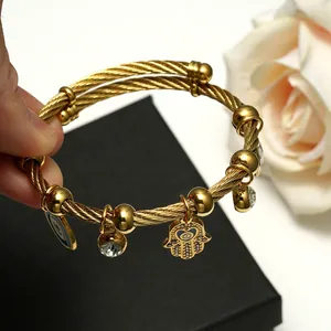 Golden stainless steel wire rope bangle with Hamsa Hand and Evil Eye charms on black box