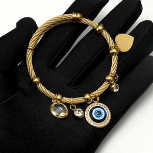 Macro detail of gold-braided steel bracelet with evil eye and heart charms on black glove