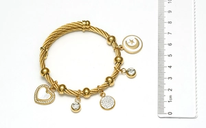 Détail du bracelet câble doré avec breloques cœur et étoile à côté d'une règle